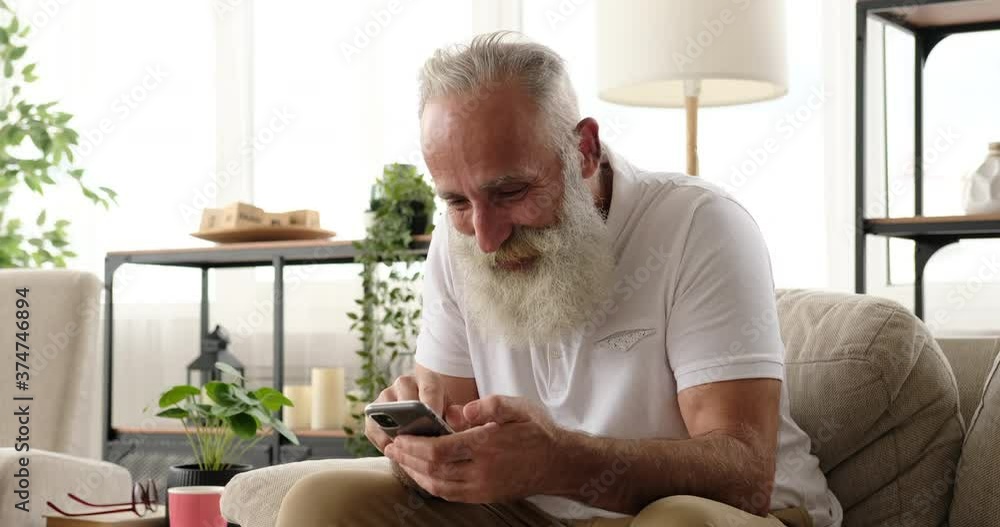 Senior man pleased on receiving good news using mobile phone at home Senior man pleased on receiving good news using mobile phone at home