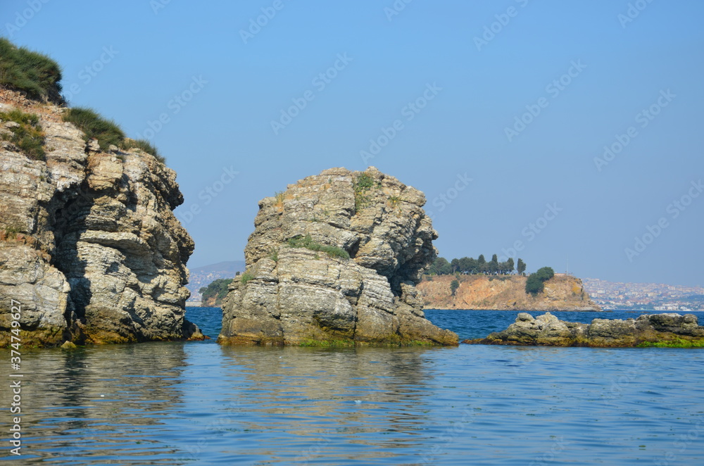 Sea view of one of the islands in the Aegean Sea. The other island visible behind the cliffs around the island. The city visible behind cliffs and islands. Herbs and mosses scattered over the cliffs. 