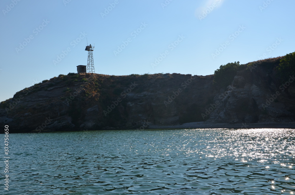 The view of an island in the Aegean Sea from the sea with backlight and the reflection of sunlight from the sea surface. A small bay overshadowed by the island. Wireless set on top of the island.