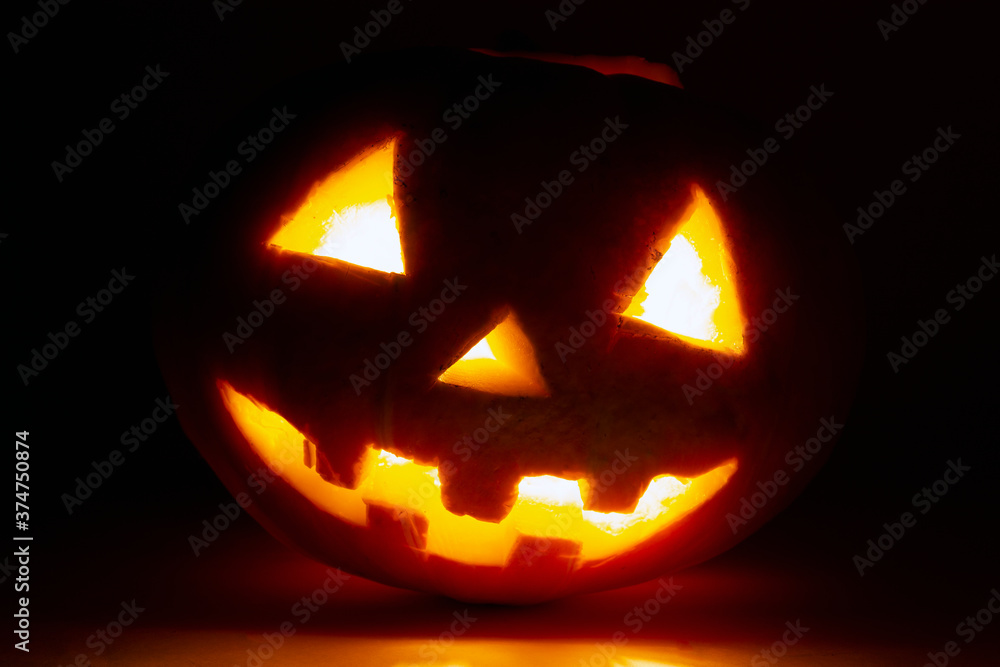 Fototapeta premium straszna twarz dyni na halloween w ciemnym pokoju świeca pali się w środku na świąteczne dekoracje, pocztówki i lokale