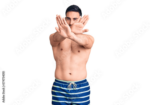 Young handsome man wearing swimwear rejection expression crossing arms and palms doing negative sign  angry face