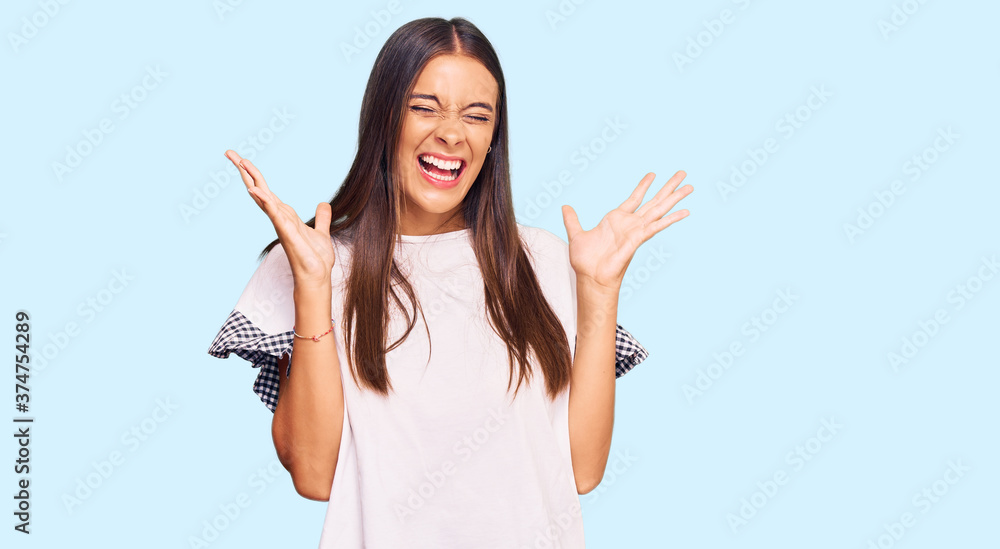 Young hispanic woman wearing casual clothes celebrating mad and crazy for success with arms raised and closed eyes screaming excited. winner concept Young hispanic woman wearing casual clothes celebrating mad and crazy for success with arms raised and closed eyes screaming excited. winner concept