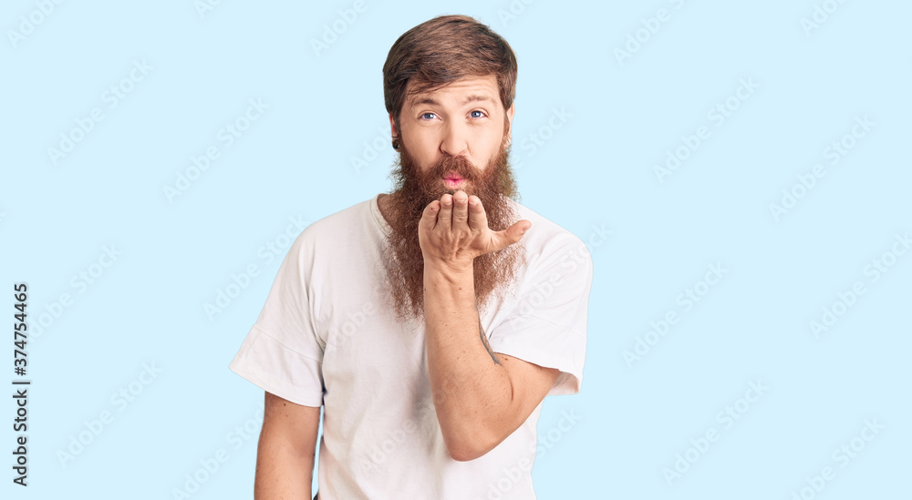 Handsome young red head man with long beard wearing casual white tshirt looking at the camera blowing a kiss with hand on air being lovely and sexy. love expression. Handsome young red head man with long beard wearing casual white tshirt looking at the camera blowing a kiss with hand on air being lovely and sexy. love expression.