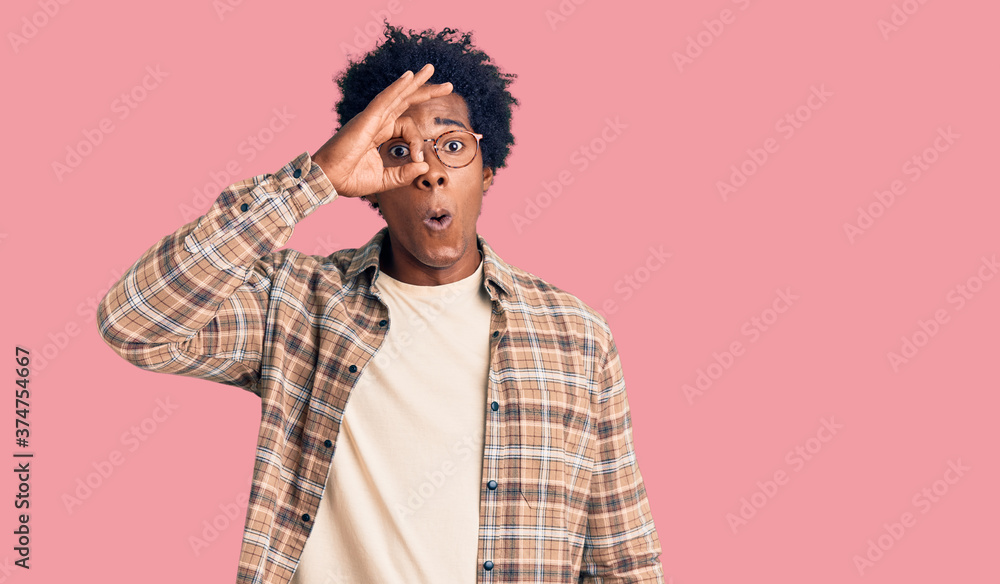 Handsome african american man with afro hair wearing casual clothes and glasses doing ok gesture shocked with surprised face, eye looking through fingers. unbelieving expression. Handsome african american man with afro hair wearing casual clothes and glasses doing ok gesture shocked with surprised face, eye looking through fingers. unbelieving expression.