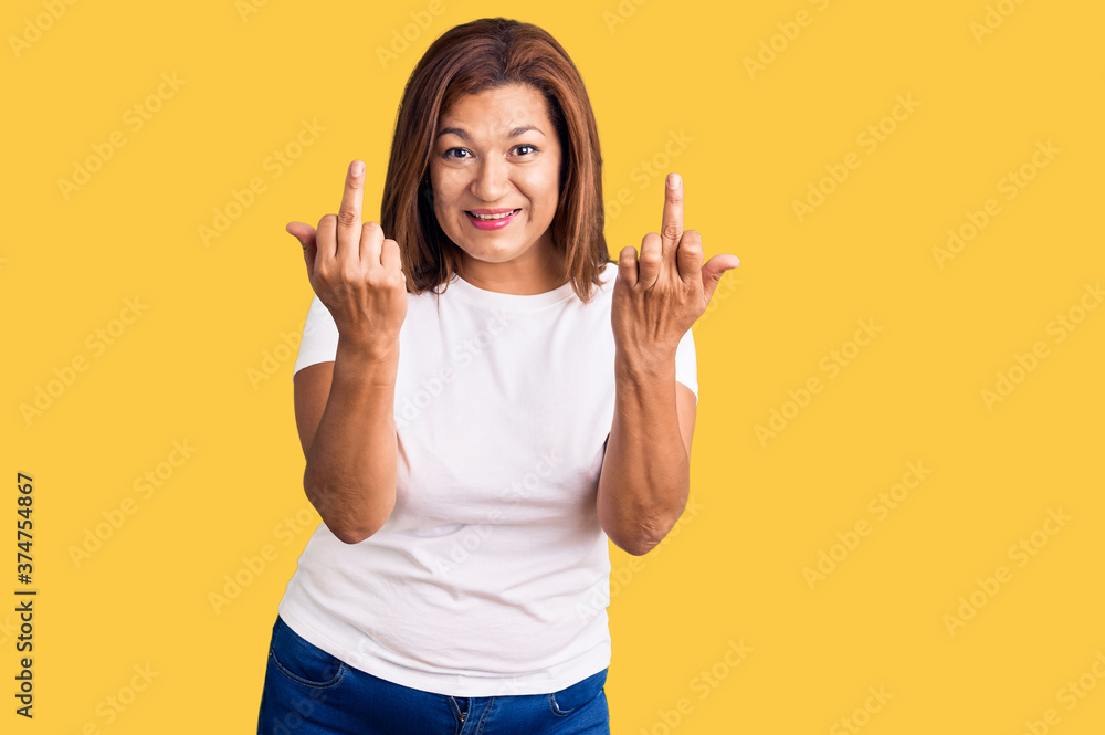 Middle age latin woman wearing casual white tshirt showing middle finger doing fuck you bad expression, provocation and rude attitude. screaming excited Middle age latin woman wearing casual white tshirt showing middle finger doing fuck you bad expression, provocation and rude attitude. screaming excited