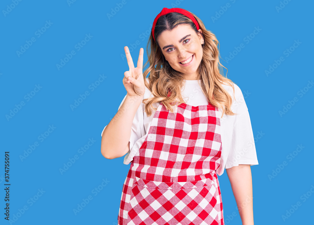 Young caucasian woman wearing apron showing and pointing up with fingers number two while smiling confident and happy. Young caucasian woman wearing apron showing and pointing up with fingers number two while smiling confident and happy.