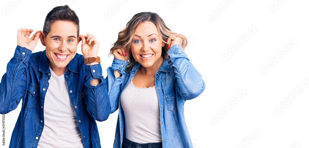 Obraz premium Couple of women wearing casual clothes smiling pulling ears with fingers, funny gesture. audition problem
