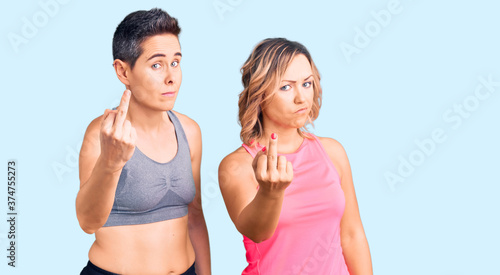 Couple of women wearing sportswear showing middle finger  impolite and rude fuck off expression