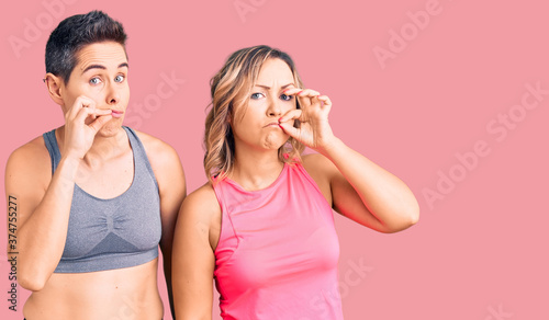 Couple of women wearing sportswear mouth and lips shut as zip with fingers. secret and silent, taboo talking