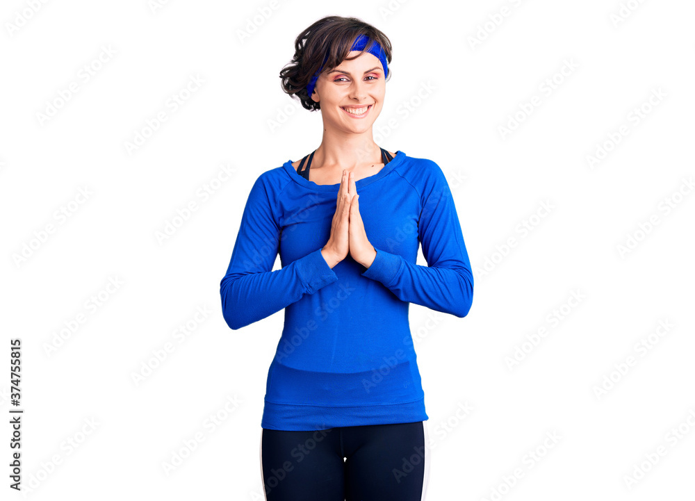 Beautiful young woman with short hair wearing training workout clothes praying with hands together asking for forgiveness smiling confident. Beautiful young woman with short hair wearing training workout clothes praying with hands together asking for forgiveness smiling confident.