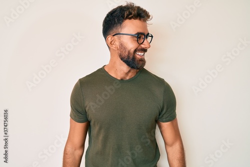 Young hispanic man wearing casual clothes and glasses looking away to side with smile on face, natural expression. laughing confident.
