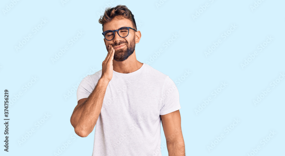 Young hispanic man wearing casual clothes and glasses touching mouth with hand with painful expression because of toothache or dental illness on teeth. dentist Young hispanic man wearing casual clothes and glasses touching mouth with hand with painful expression because of toothache or dental illness on teeth. dentist