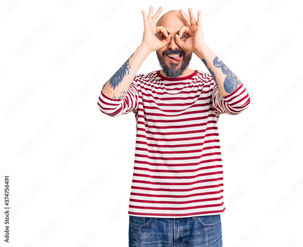Young handsome man wearing casual clothes doing ok gesture like binoculars sticking tongue out, eyes looking through fingers. crazy expression. Young handsome man wearing casual clothes doing ok gesture like binoculars sticking tongue out, eyes looking through fingers. crazy expression.