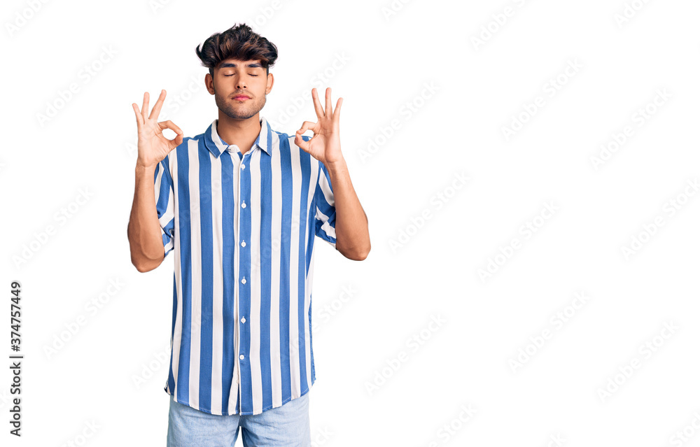 Young hispanic man wearing casual clothes relaxed and smiling with eyes closed doing meditation gesture with fingers. yoga concept. Young hispanic man wearing casual clothes relaxed and smiling with eyes closed doing meditation gesture with fingers. yoga concept.