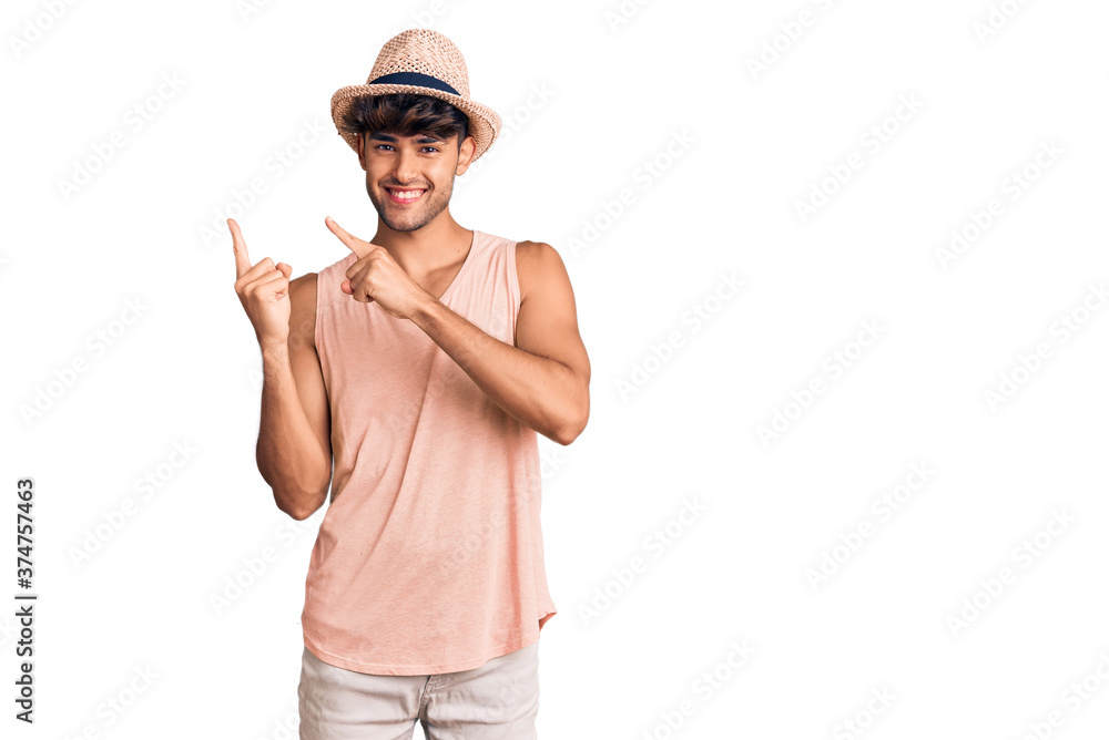 Young hispanic man wearing summer hat smiling and looking at the camera pointing with two hands and fingers to the side. Young hispanic man wearing summer hat smiling and looking at the camera pointing with two hands and fingers to the side.