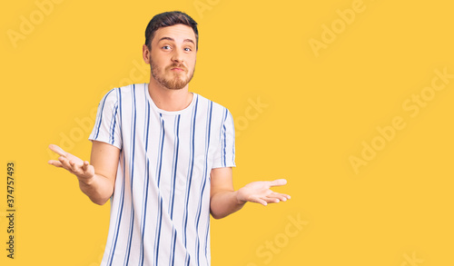 Konstfotografi Handsome young man with bear wearing casual clothes clueless and confused expression with arms and hands raised