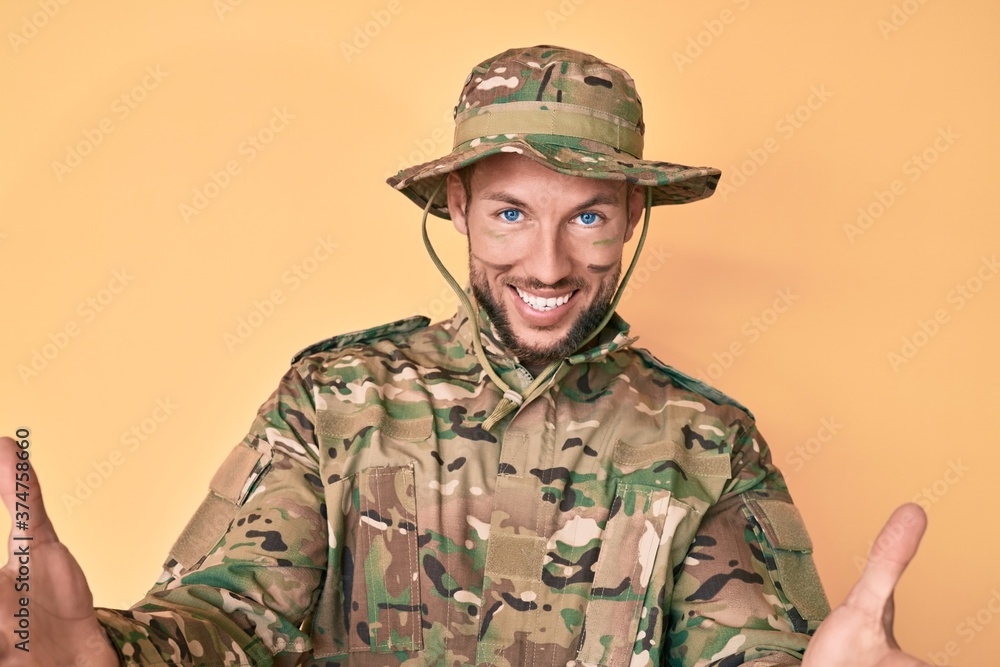 Young caucasian man wearing camouflage army uniform looking at the camera smiling with open arms for hug. cheerful expression embracing happiness. Young caucasian man wearing camouflage army uniform looking at the camera smiling with open arms for hug. cheerful expression embracing happiness.