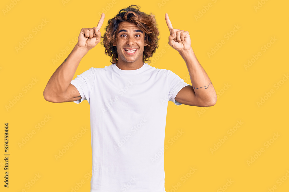 Young hispanic man wearing casual white tshirt smiling amazed and surprised and pointing up with fingers and raised arms.