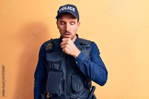 Young handsome policeman wearing police uniform and bulletprof over yellow background feeling unwell and coughing as symptom for cold or bronchitis. Health care concept. photo