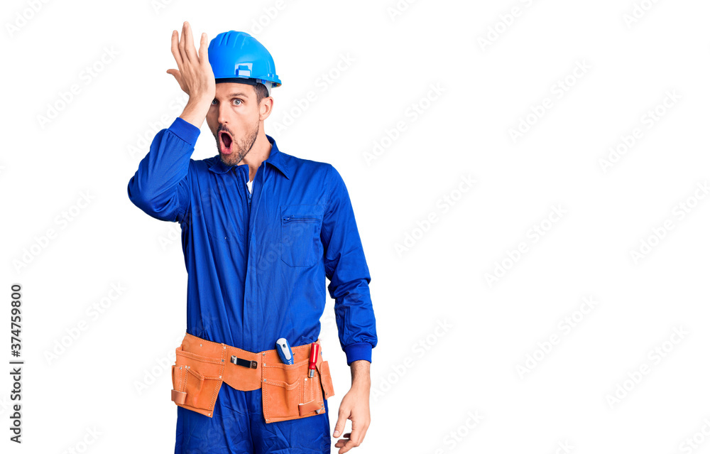 Young handsome man wearing worker uniform and hardhat surprised with hand on head for mistake, remember error. forgot, bad memory concept.