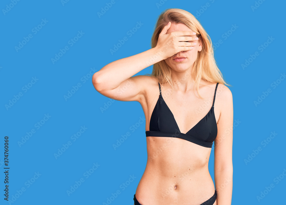 Young beautiful blonde woman wearing bikini covering eyes with hand, looking serious and sad. sightless, hiding and rejection concept Young beautiful blonde woman wearing bikini covering eyes with hand, looking serious and sad. sightless, hiding and rejection concept