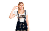 Young beautiful blonde woman wearing oktoberfest dress smiling and confident gesturing with hand doing small size sign with fingers looking and the camera. measure concept.