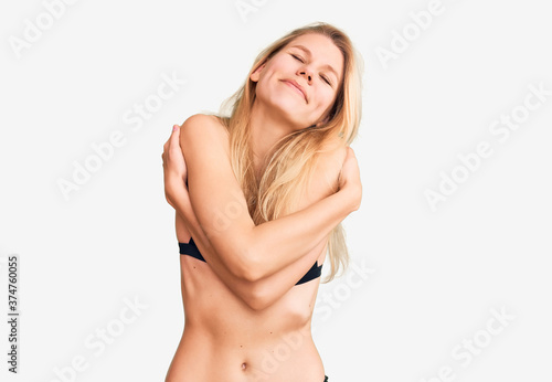 Young beautiful blonde woman wearing bikini hugging oneself happy and positive, smiling confident. self love and self care © Krakenimages.com