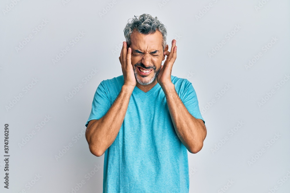 Middle age grey-haired man wearing casual clothes covering ears with fingers with annoyed expression for the noise of loud music. deaf concept. Middle age grey-haired man wearing casual clothes covering ears with fingers with annoyed expression for the noise of loud music. deaf concept.
