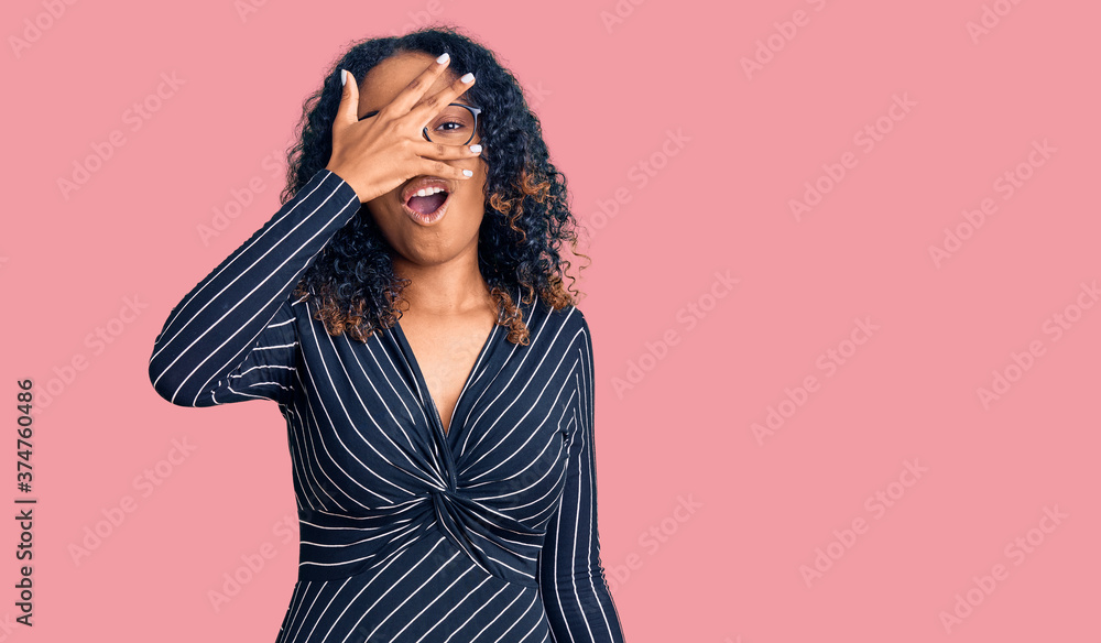 Young african american woman wearing casual clothes and glasses peeking in shock covering face and eyes with hand, looking through fingers with embarrassed expression. Young african american woman wearing casual clothes and glasses peeking in shock covering face and eyes with hand, looking through fingers with embarrassed expression.