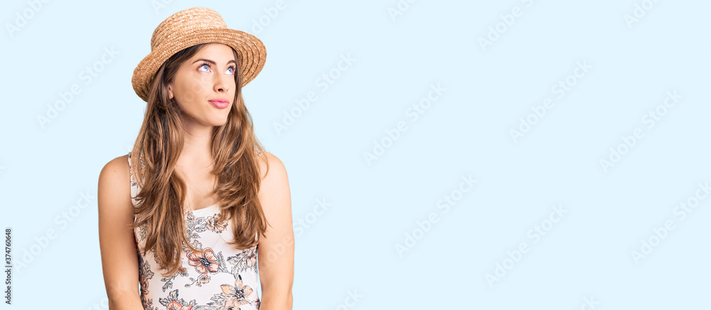 Beautiful caucasian young woman wearing summer hat smiling looking to the side and staring away thinking.