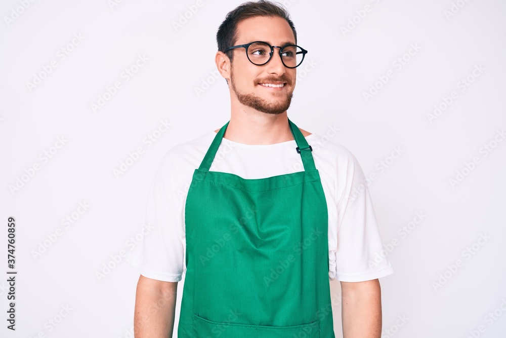 Young handsome man wearing apron looking to side, relax profile pose with natural face and confident smile. Young handsome man wearing apron looking to side, relax profile pose with natural face and confident smile.