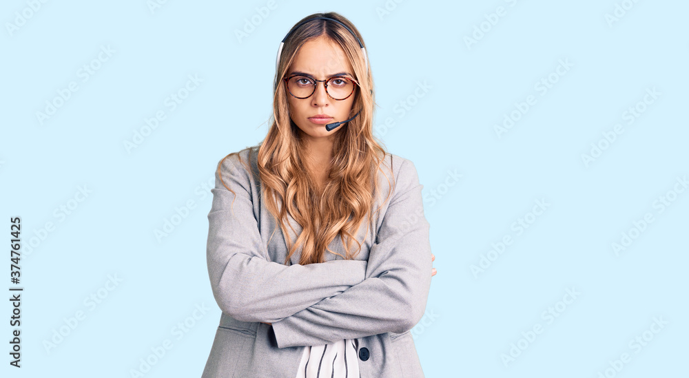 Young beautiful blonde woman wearing call center agent headset skeptic and nervous, disapproving expression on face with crossed arms. negative person.