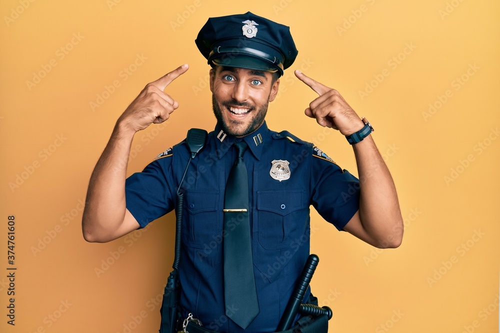 Handsome hispanic man wearing police uniform smiling pointing to head with both hands finger, great idea or thought, good memory Handsome hispanic man wearing police uniform smiling pointing to head with both hands finger, great idea or thought, good memory