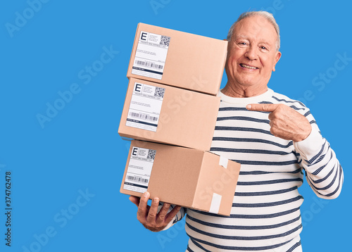 Senior handsome grey-haired man holding delivery boxes smiling happy pointing with hand and finger