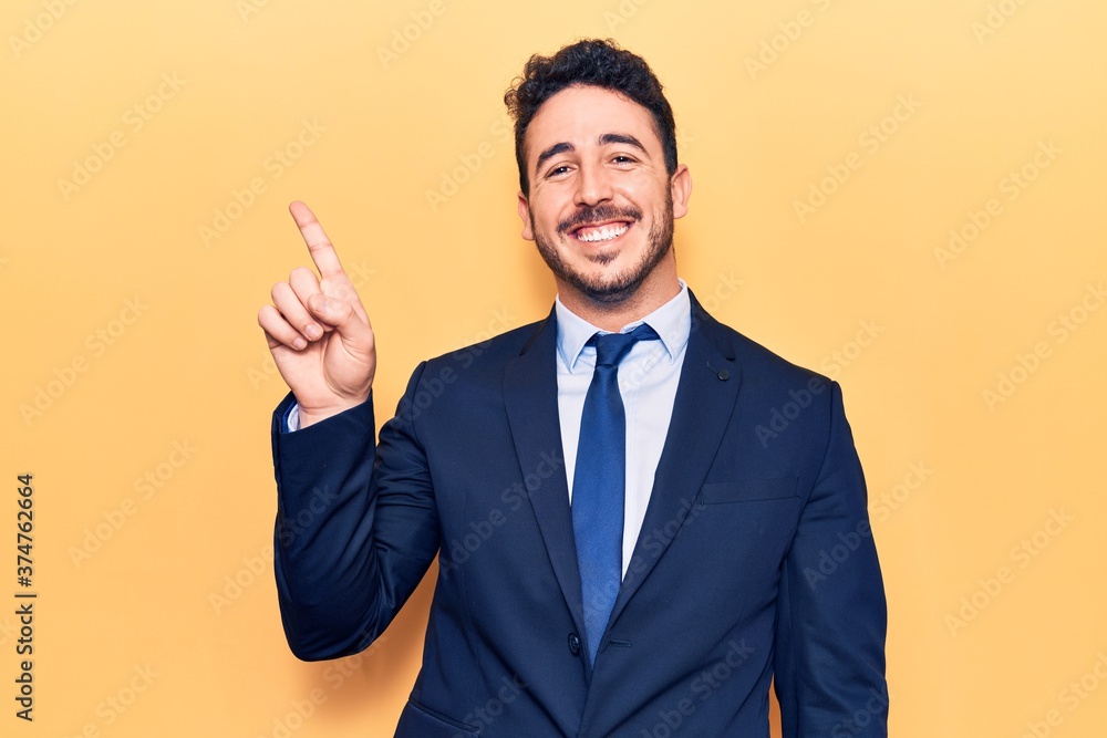 Young hispanic man wearing suit showing and pointing up with finger number one while smiling confident and happy. Young hispanic man wearing suit showing and pointing up with finger number one while smiling confident and happy.