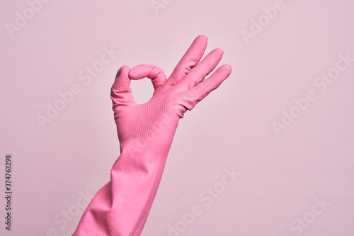 Hand of caucasian young man with cleaning glove over isolated pink background gesturing approval expression doing okay symbol with fingers