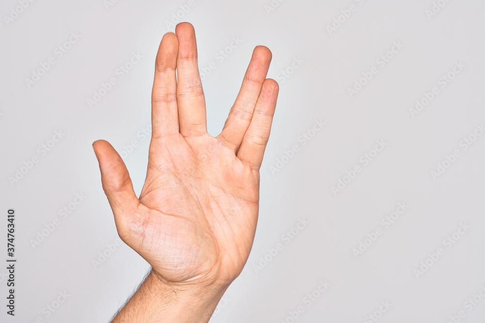 Hand of caucasian young man showing fingers over isolated white background greeting doing Vulcan salute, showing hand palm and fingers, freak culture Hand of caucasian young man showing fingers over isolated white background greeting doing Vulcan salute, showing hand palm and fingers, freak culture