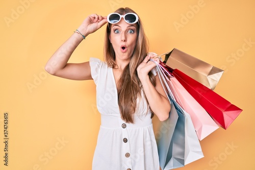 Young blonde girl holding shopping bags afraid and shocked with surprise and amazed expression, fear and excited face.
