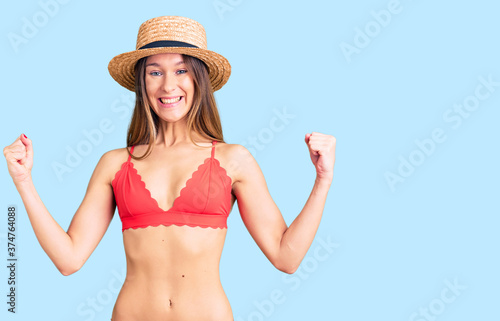 Beautiful brunette young woman wearing bikini celebrating surprised and amazed for success with arms raised and open eyes. winner concept.