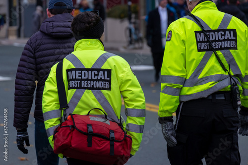 Medical first responders walking along a road wearing black wool stocking caps, yellow reflective coats with medical first responder in grey letters.