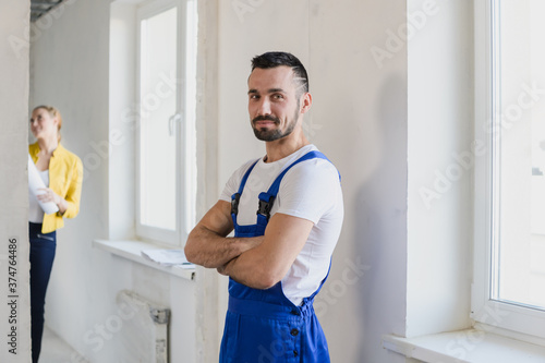 A man in blue overalls stands in a renovated apartment. The customer stands in the background