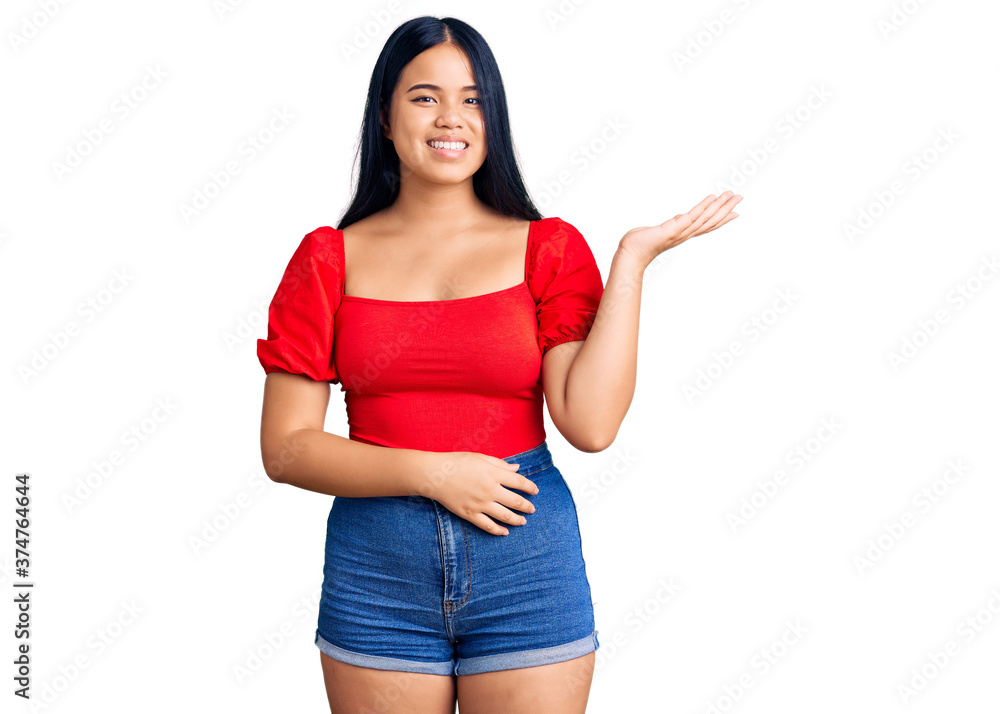 Young beautiful asian girl wearing casual clothes smiling cheerful presenting and pointing with palm of hand looking at the camera. Young beautiful asian girl wearing casual clothes smiling cheerful presenting and pointing with palm of hand looking at the camera.