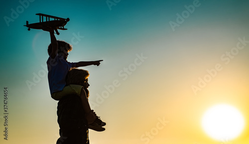 Success and child leader concept. Sunset silhouette of Father and son together. Boy child is sitting on daddy shoulder piggyback while the flight.