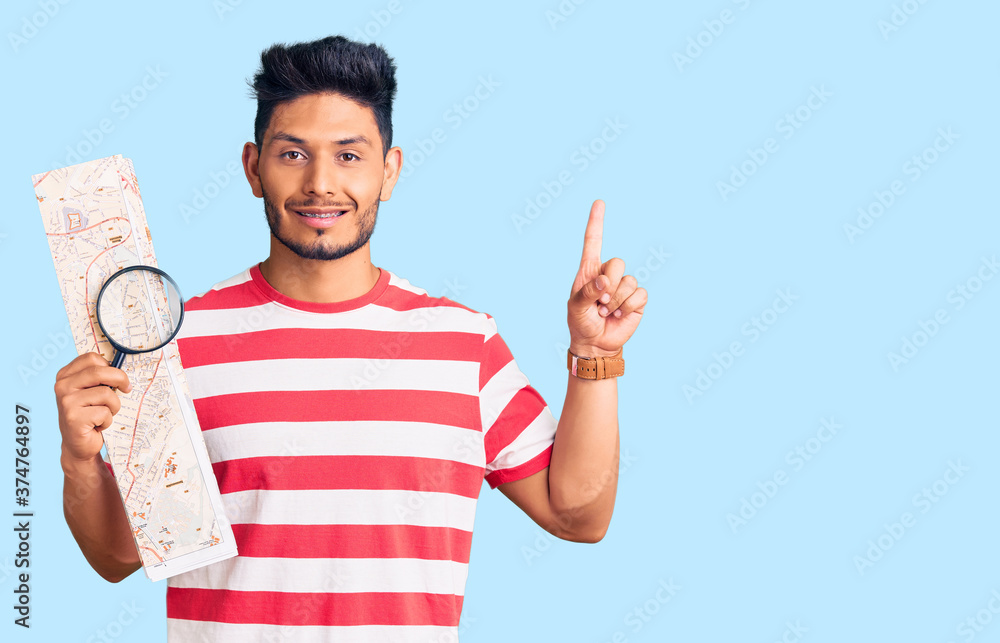 Handsome latin american young man looking at city map with magnifying glass surprised with an idea or question pointing finger with happy face, number one Handsome latin american young man looking at city map with magnifying glass surprised with an idea or question pointing finger with happy face, number one