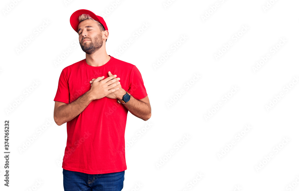 Young handsome blond man wearing t-shirt and cap smiling with hands on chest with closed eyes and grateful gesture on face. health concept.