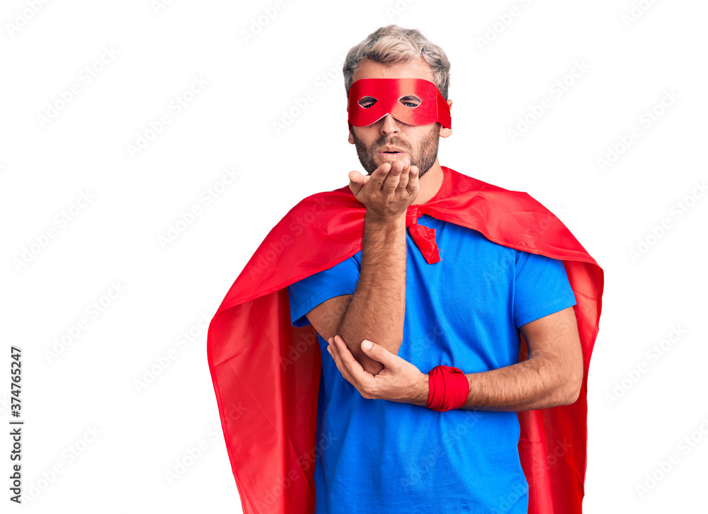 Young blond man wearing super hero custome looking at the camera blowing a kiss with hand on air being lovely and sexy. love expression. Young blond man wearing super hero custome looking at the camera blowing a kiss with hand on air being lovely and sexy. love expression.