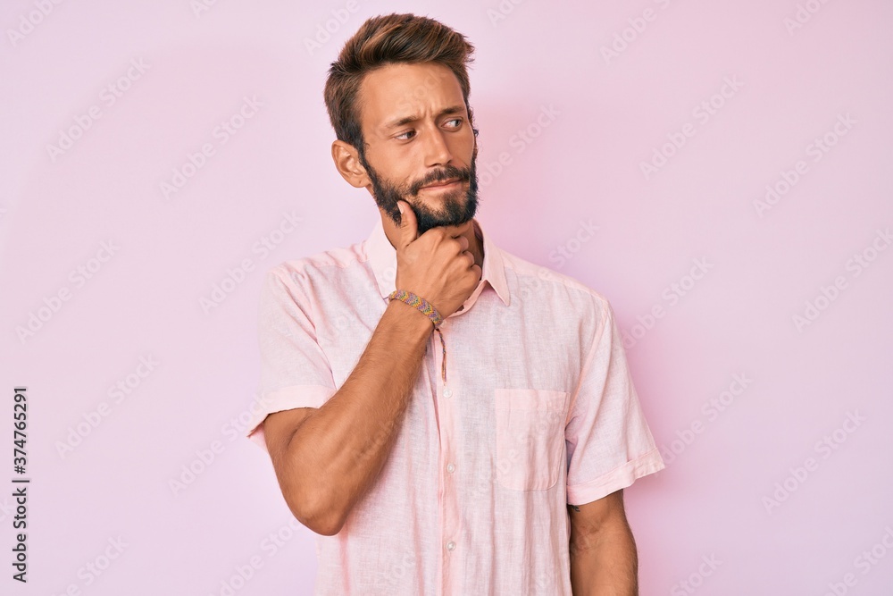 Handsome caucasian man with beard wearing casual pink shirt serious face thinking about question with hand on chin, thoughtful about confusing idea Handsome caucasian man with beard wearing casual pink shirt serious face thinking about question with hand on chin, thoughtful about confusing idea