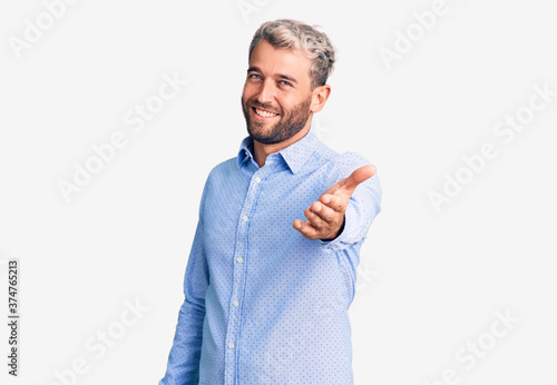 Young handsome blond man wearing elegant shirt smiling cheerful offering palm hand giving assistance and acceptance.