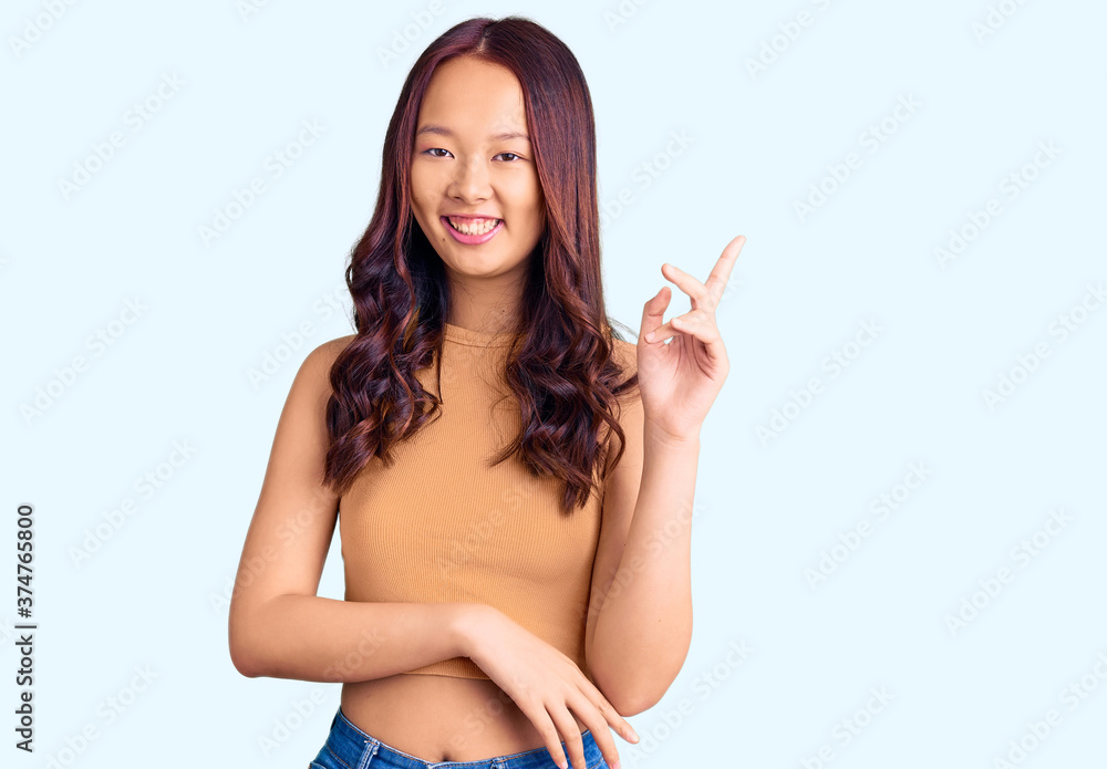 Young beautiful chinese girl wearing casual clothes smiling happy pointing with hand and finger to the side Young beautiful chinese girl wearing casual clothes smiling happy pointing with hand and finger to the side
