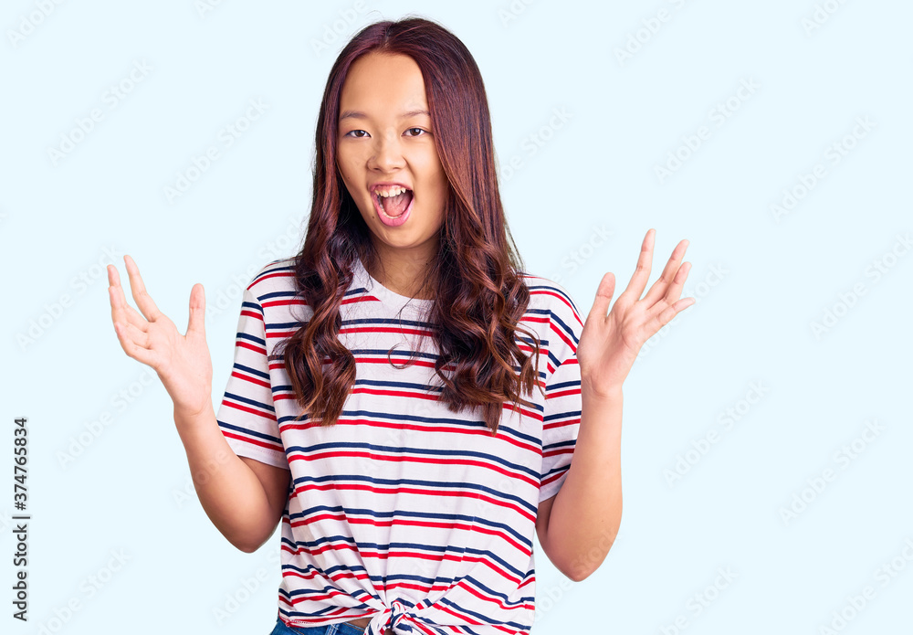 Young beautiful chinese girl wearing casual clothes celebrating victory with happy smile and winner expression with raised hands Young beautiful chinese girl wearing casual clothes celebrating victory with happy smile and winner expression with raised hands